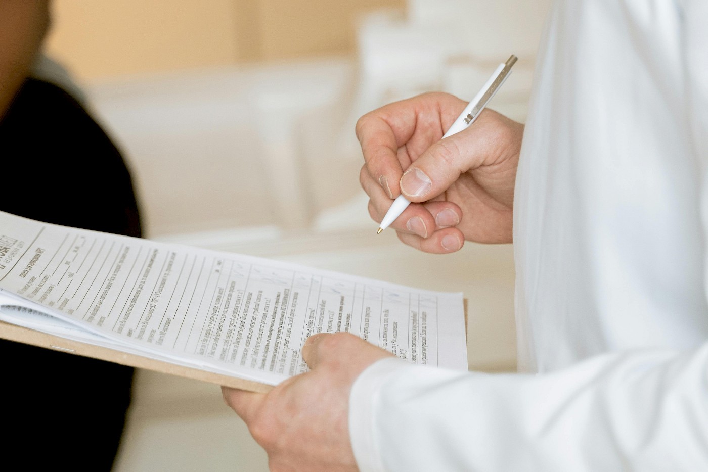 close up of doctor in white coat holding pen and clipboard
